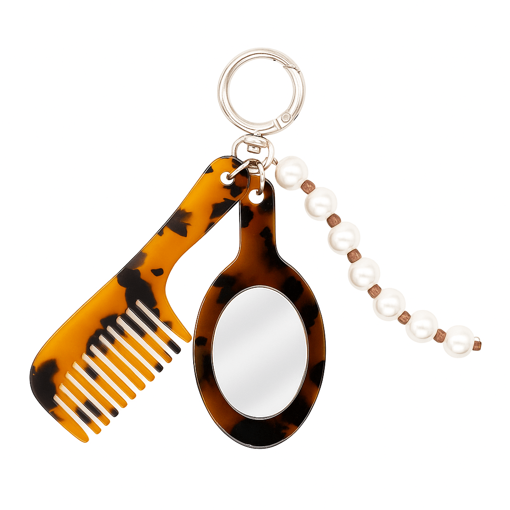 Charm con tres colgantes: un peine tamaño mini, un espejo y una cuerda trenzada con perlas. 
Incluye una anilla circular resistente para aplicar el adaptador universal y utilizarlo en el móvil o como llavero. 
